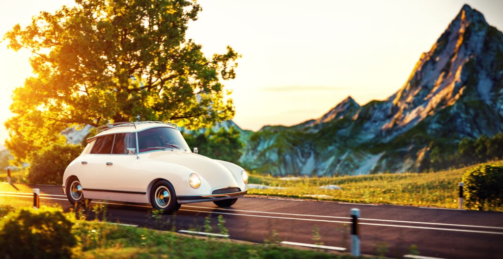 Cute little retro car goes by wonderful countryside road at sunset